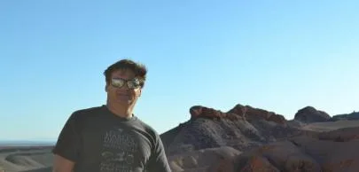 Homem sorrindo em frente a montanhas sob céu azul