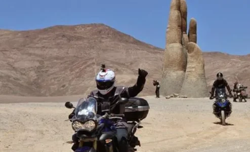 eb1d7003c8e6df756d2d2496e82e364b482d70a1 Motociclistas passando por escultura mão deserto Atacama Chile.