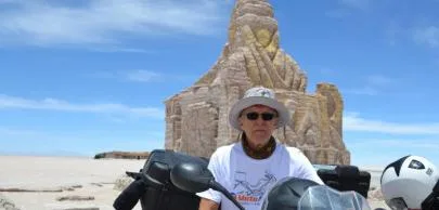 Homem de chapéu e óculos em deserto com escultura.
