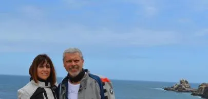 eb1d7003c8e6df756d2d2496e82e364b482d70a1 Casal sorrindo com roupas de motoqueiro à beira-mar.