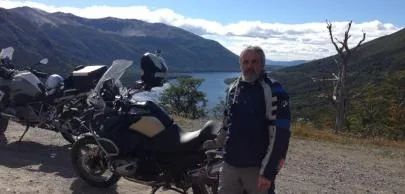 Homem ao lado de motocicleta em estrada montanhosa.