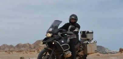 eb1d7003c8e6df756d2d2496e82e364b482d70a1 Motociclista em estrada desértica com capacete e jaqueta preta.
