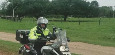 Motociclista com jaqueta amarela em estrada de terra rural.