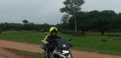 Motociclista com capacete amarelo em estrada de terra rural.