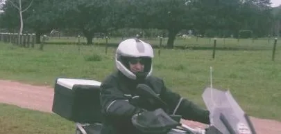 Motociclista com capacete branco em estrada rural arborizada.