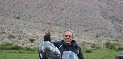 Homem em motocicleta fazendo sinal de paz em paisagem montanhosa.