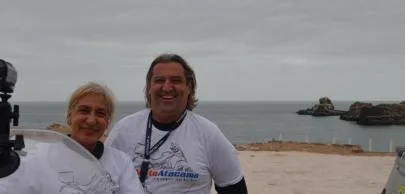 Duas pessoas sorrindo em praia com céu nublado.