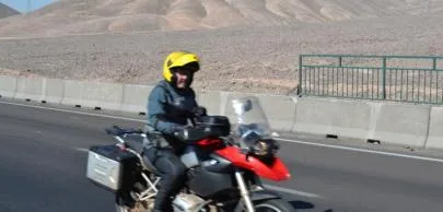 Motociclista com capacete amarelo em estrada deserta montanhosa