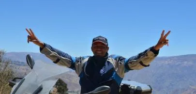 Motociclista sorridente faz sinal de paz em estrada montanhosa