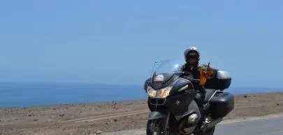 Motociclista em estrada costeira deserta sob céu azul claro.