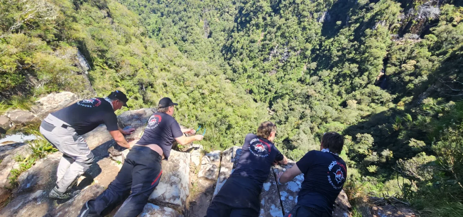 Quatro homens observando penhasco coberto por vegetação densa.