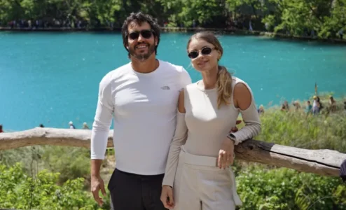 eb1d7003c8e6df756d2d2496e82e364b482d70a1 Casal sorrindo em frente a lago azul e árvores.