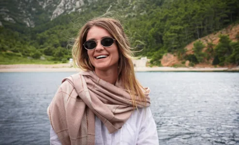 eb1d7003c8e6df756d2d2496e82e364b482d70a1 Mulher sorrindo com óculos de sol em frente ao lago.