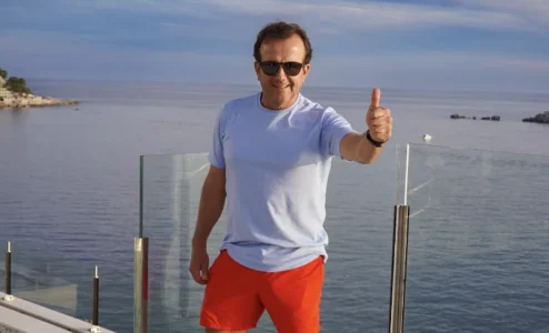 eb1d7003c8e6df756d2d2496e82e364b482d70a1 Homem sorrindo com óculos de sol e bermuda vermelha.