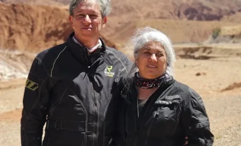 Casal de jaquetas pretas em paisagem desértica montanhosa.