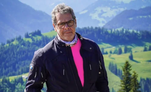 Homem de jaqueta preta em paisagem montanhosa nevada.