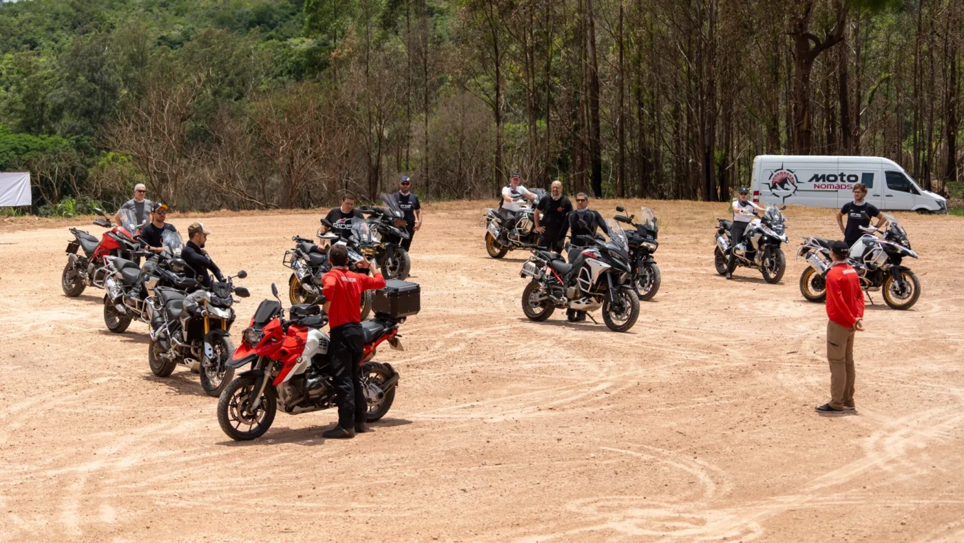 Grupo de motociclistas reunidos em campo aberto com instrutores.