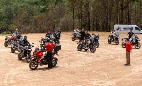 Grupo de motociclistas reunidos em campo aberto com instrutores.