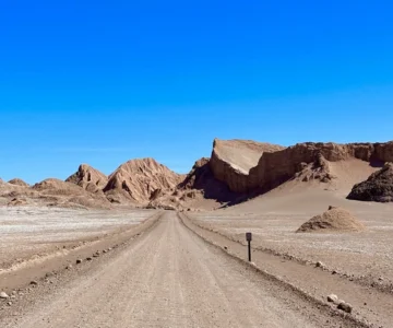 eb1d7003c8e6df756d2d2496e82e364b482d70a1 Estrada deserta cercada por montanhas rochosas sob céu azul